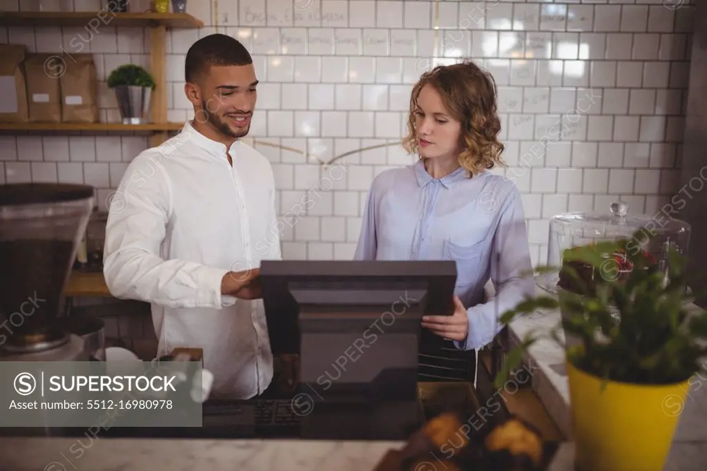 Male owner with waitress using computer at counter in coffee shop