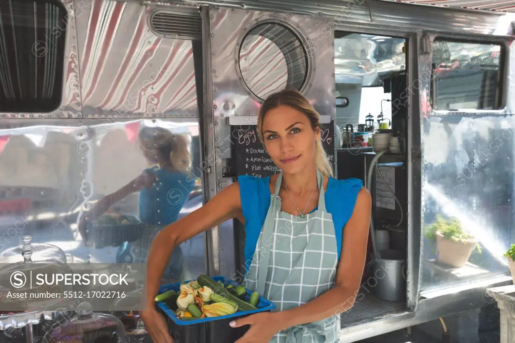 Female waitress holding vegetables in basket near food truck