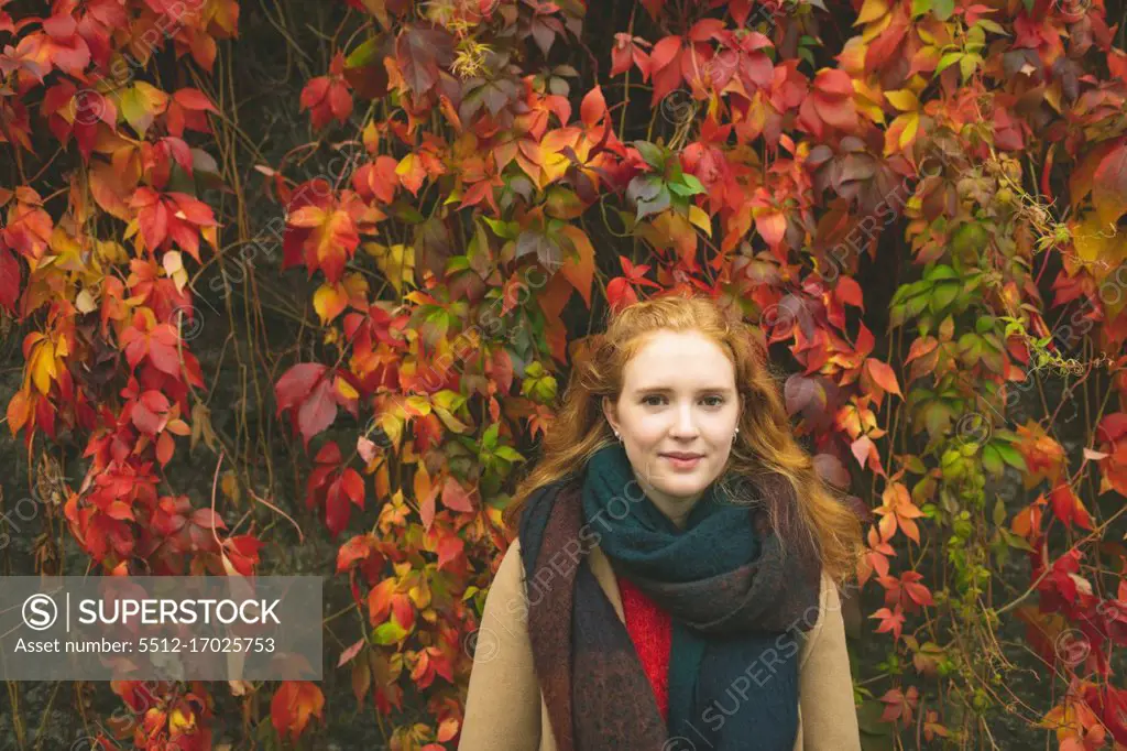Redhead woman standing against plant creeper during autumn