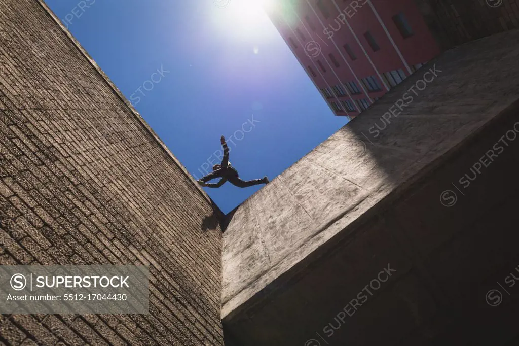 Side low angle view of a Caucasian man practicing parkour by the building in a city on a sunny day, jumping on the rooftop.