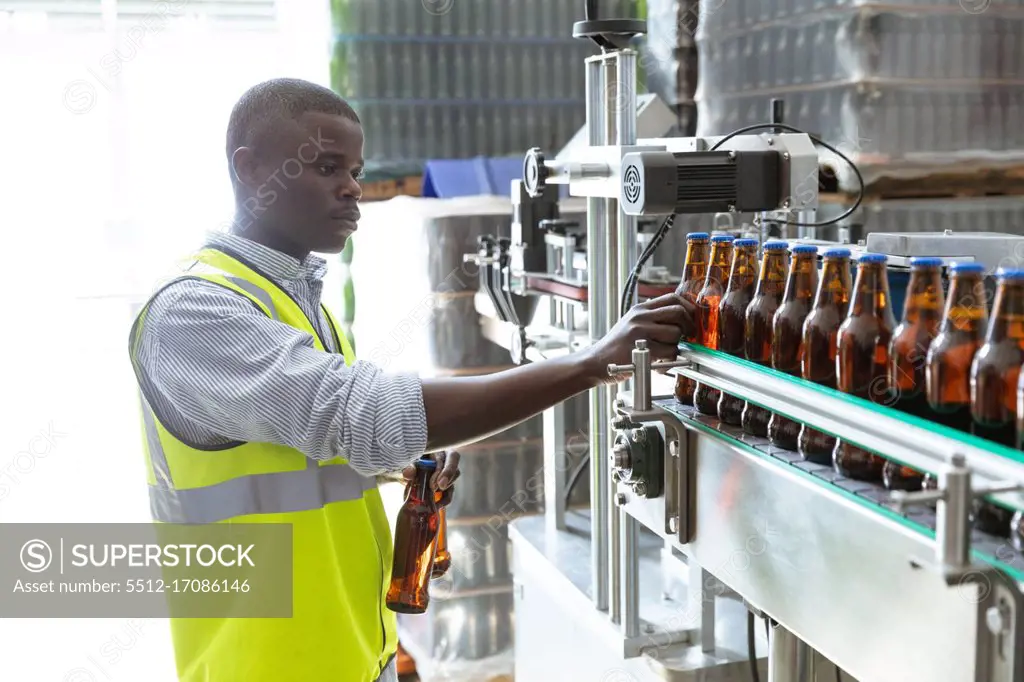 African American man worker working in a brewery, inspecting the bottles at a conveyor belt. Manufacturing and beer brewery. 