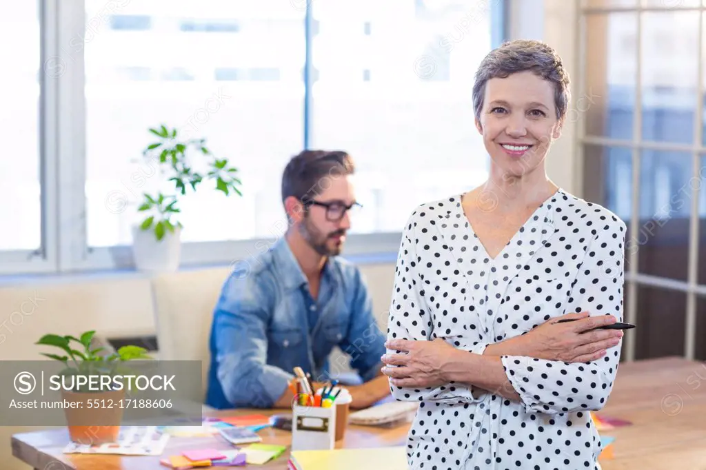 Smiling woman standing arms crossed with her partner behind in the office