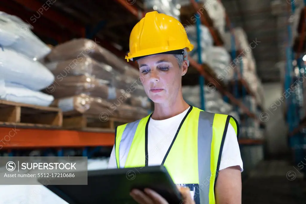 Front view of Caucasian Attentive female staff using digital tablet in warehouse. This is a freight transportation and distribution warehouse. Industrial and industrial workers concept