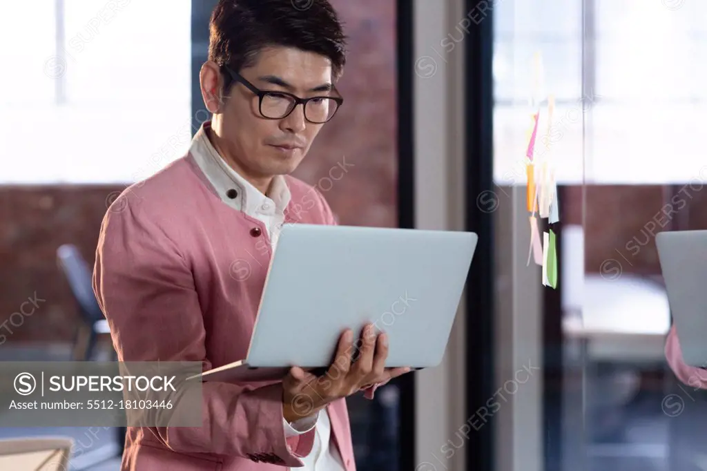 Stylish asian businessman standing and using laptop computer. business person at work in modern office.