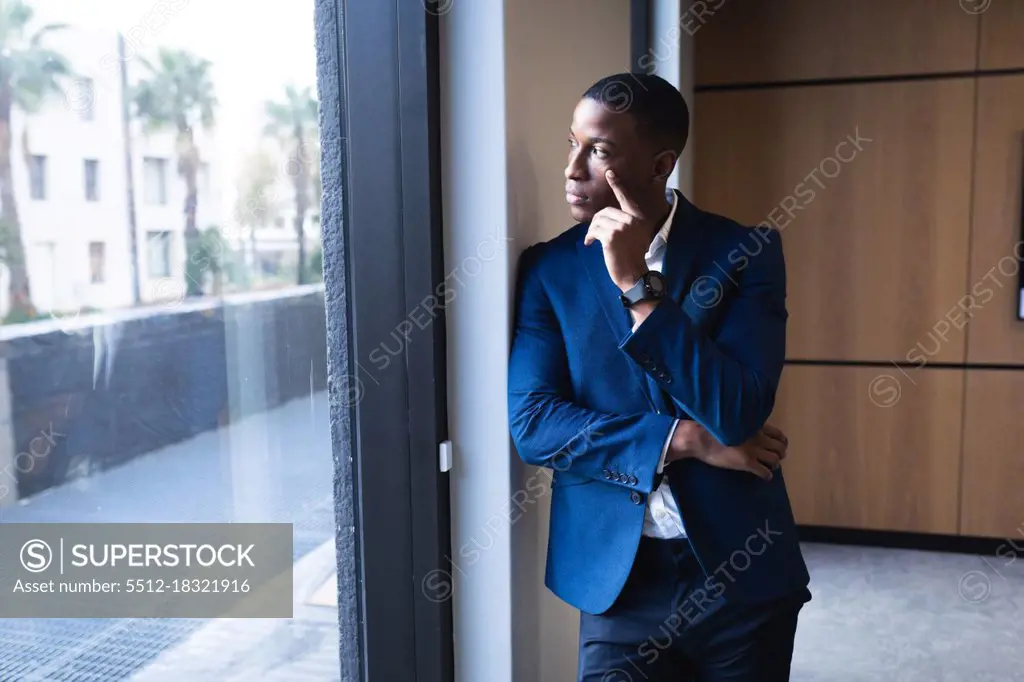 Thoughtful african american businessman looking out of window at modern office. business and office concept