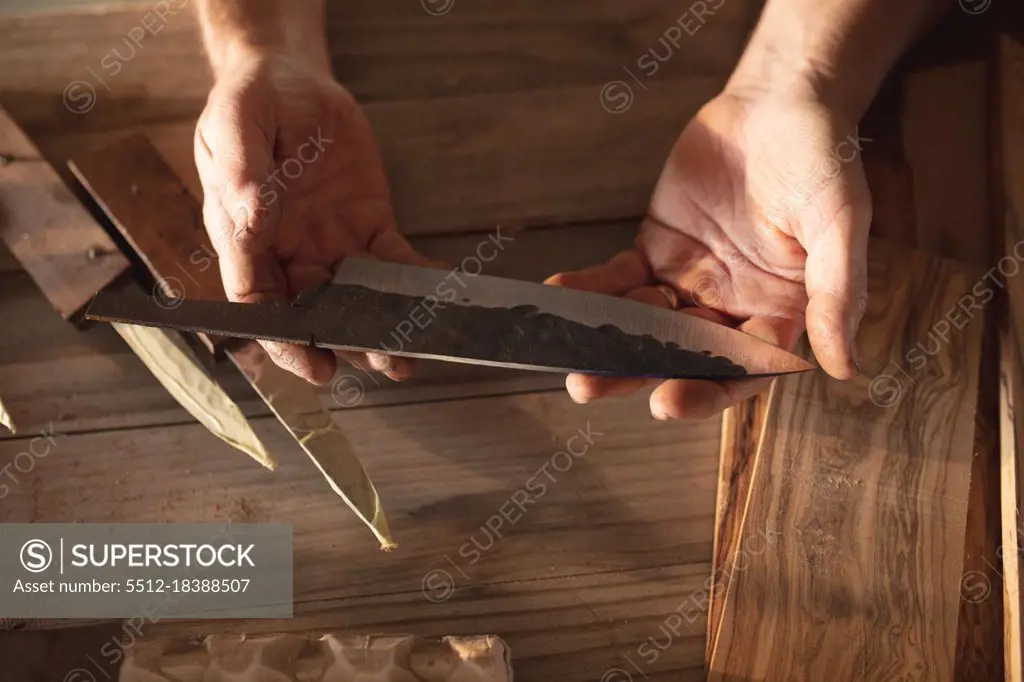 Hands of caucasian male knife maker in workshop, holding handmade knife. independent small business craftsman at work.