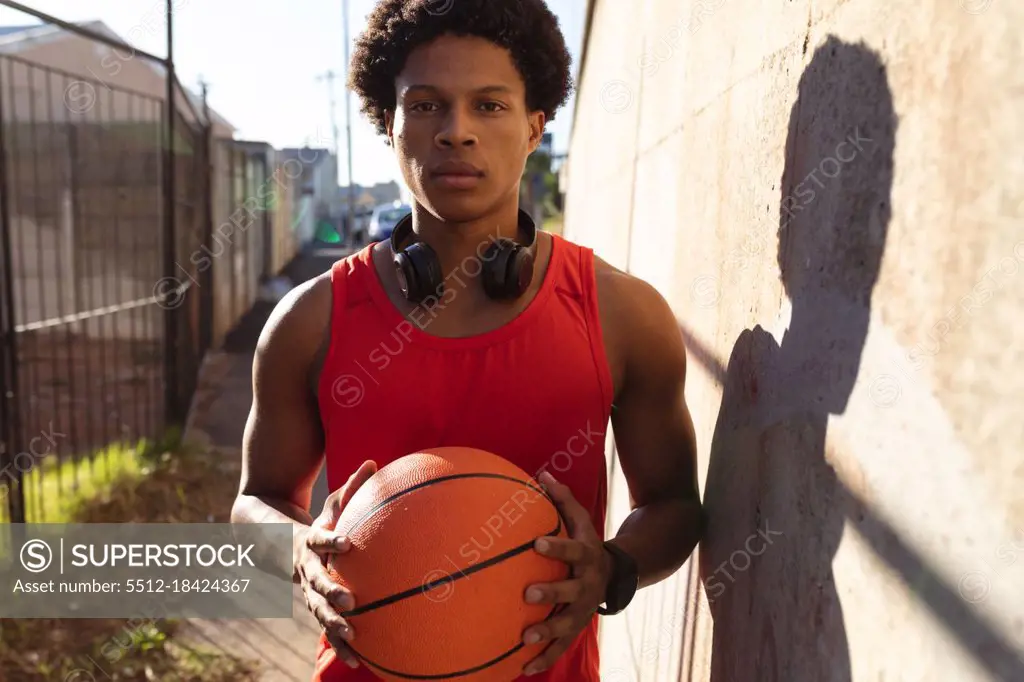 Portrait of fit african american man exercising in city holding basketball in the street. fitness and active urban outdoor lifestyle.