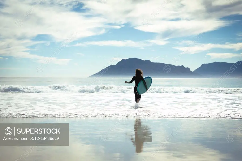 Mixed race woman holding surfboard in sea on sunny day. healthy lifestyle, enjoying leisure time outdoors.