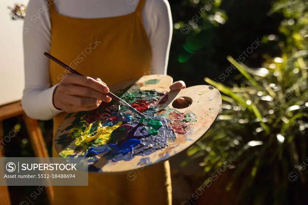 Caucasian woman in sunny garden, mixing paint on palette. domestic lifestyle, enjoying leisure time at home.