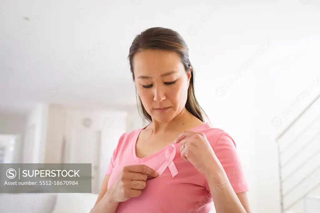 Asian woman in pink tshirt showing breast cancer awareness pink ribbon at home. health, prevention and breast cancer awareness.