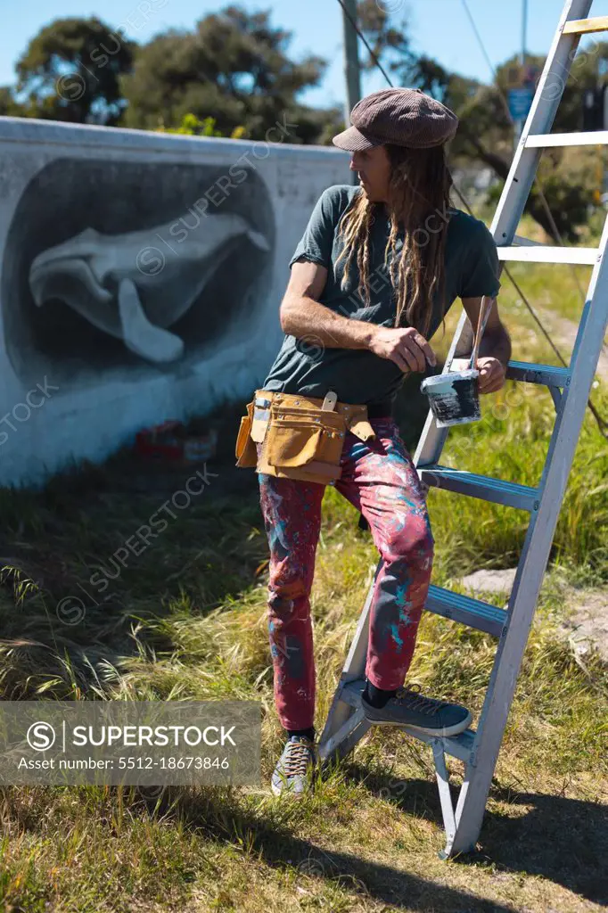 Male artist leaning on ladder while looking back at whale mural painting on wall. street art and skill.