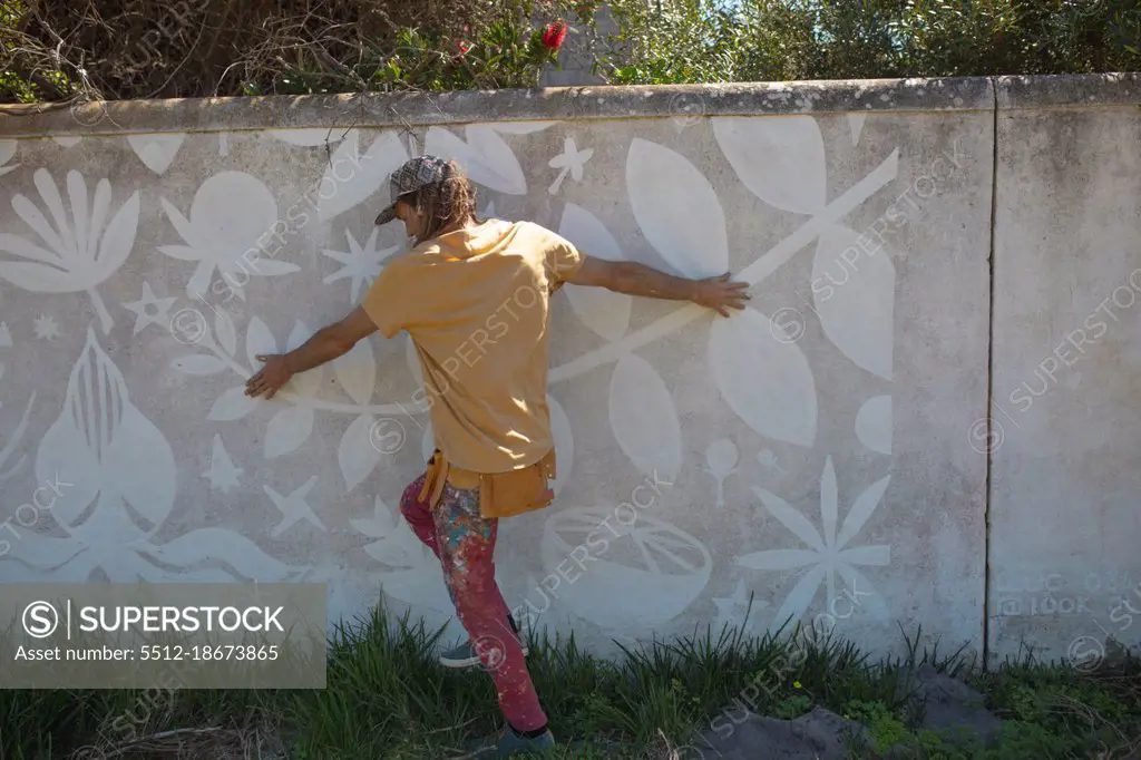 Rear view of male artist touching abstract mural painting on wall while walking on grass. street art and skill.