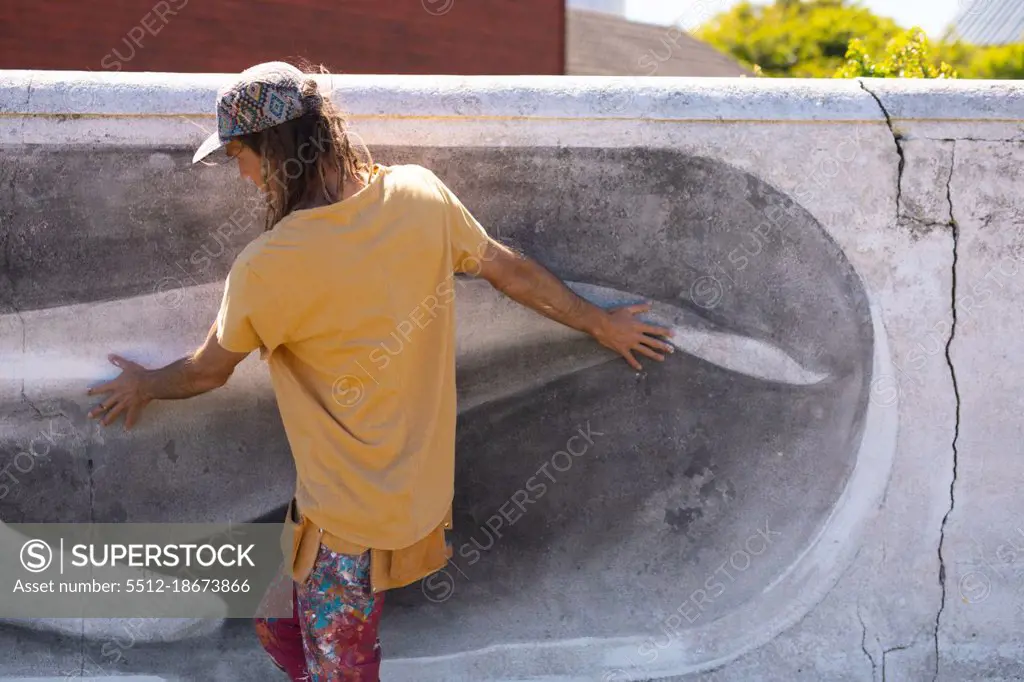 Rear view of male artist walking while touching whale mural painting on wall. street art and skill.
