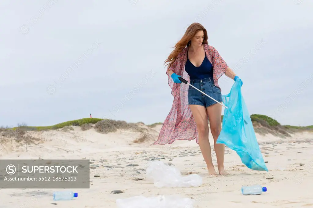 Caucasian young woman in casuals collecting plastic waste at beach. environmental cleanup, plastic pollution and responsibility.