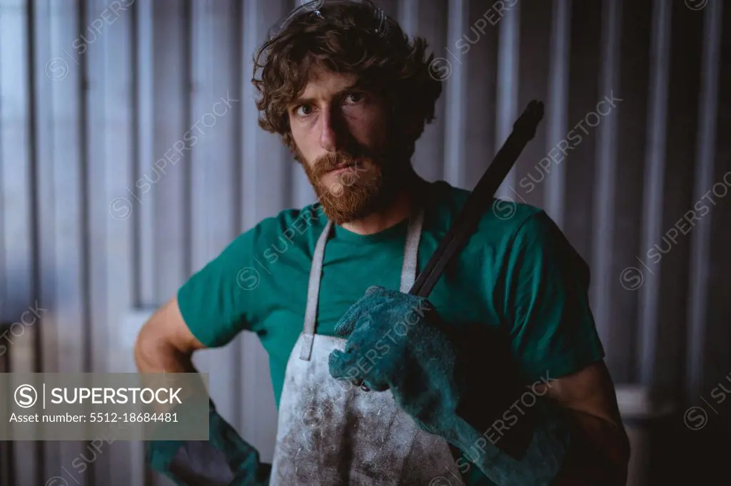 Portrait of confident bearded blacksmith holding work tool while standing in manufacturing industry. forging, metalwork and manufacturing industry.
