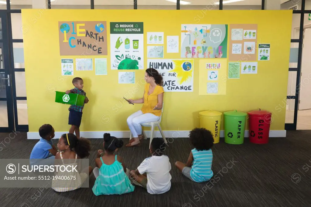 Caucasian young female teacher and african american elementary students looking at classmate. unaltered, education, environment, teaching, sustainable lifestyle and school concept.