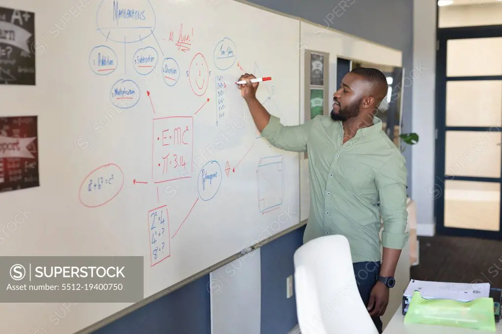 African american young male teacher writing on whiteboard while teaching in classroom. unaltered, education, teaching, occupation and school concept.