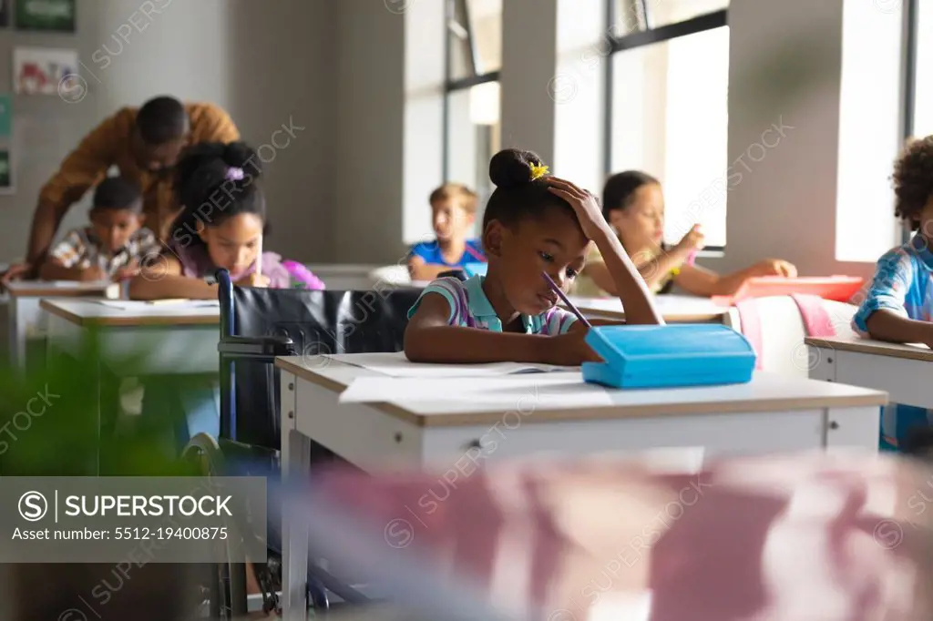 Multiracial elementary school students studying at desk in classroom. unaltered, education, childhood, disability, learning, physical disability, teaching, occupation and school concept.