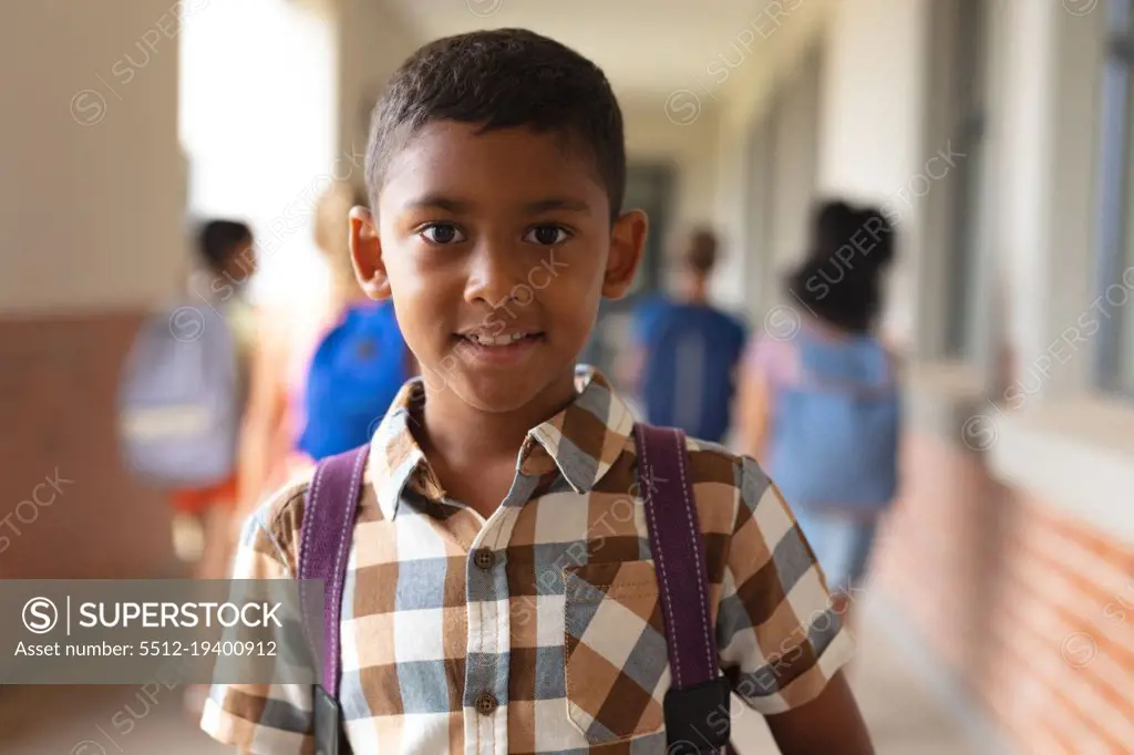 Portrait of smiling biracial elementary schoolboy standing in corridor. unaltered, education, childhood and school concept.