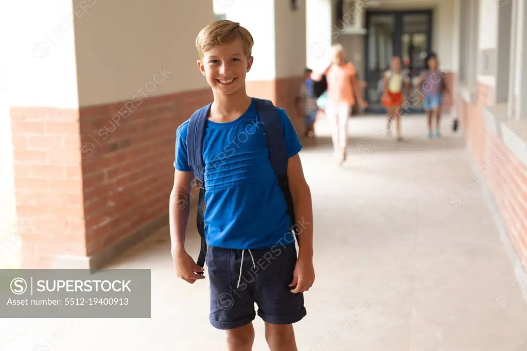 Portrait of smiling caucasian elementary schoolboy standing in corridor. unaltered, education, childhood and school concept.