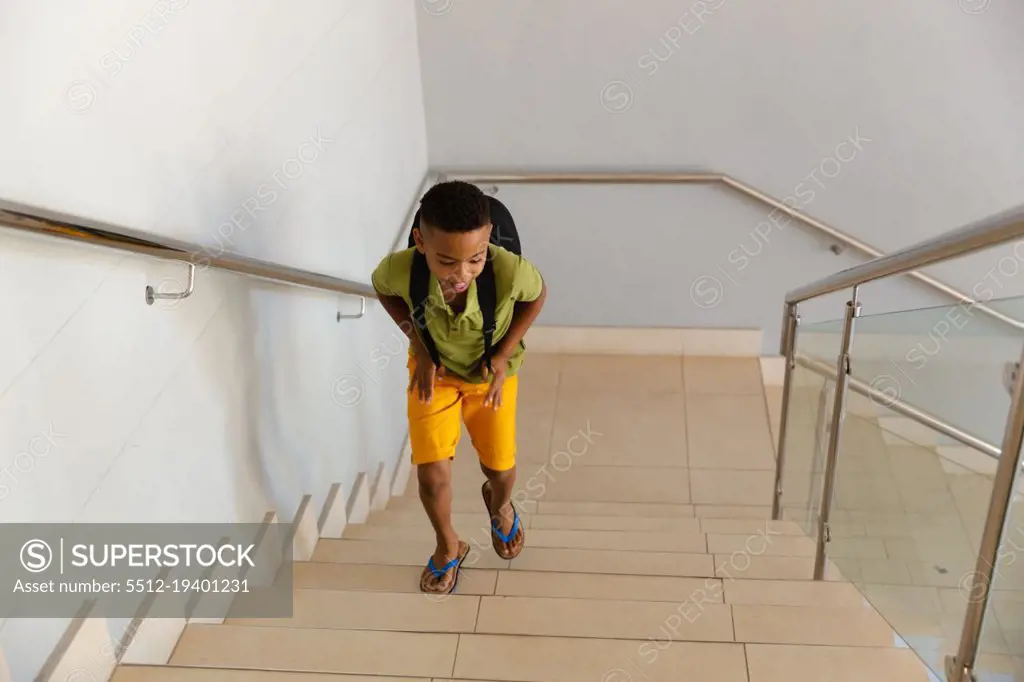 High angle view of african american elementary schoolboy with backpack climbing steps in school. unaltered, education, childhood and school concept.