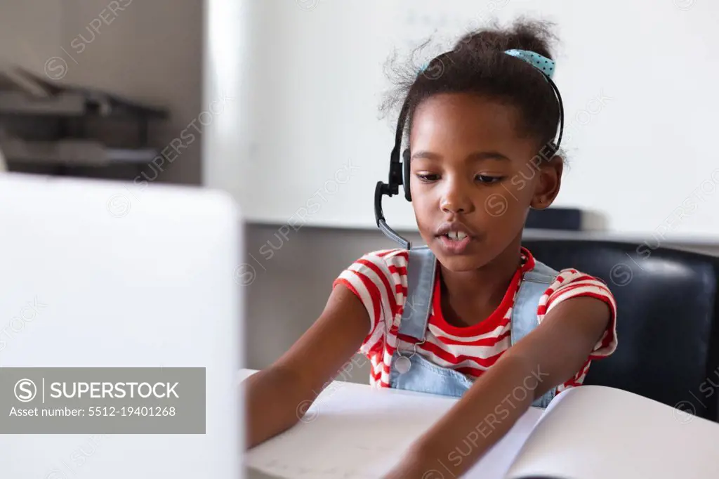 African american elementary schoolgirl wearing headphones while using laptop at desk in class. unaltered, education, listening, studying, concentration, wireless technology and school concept.