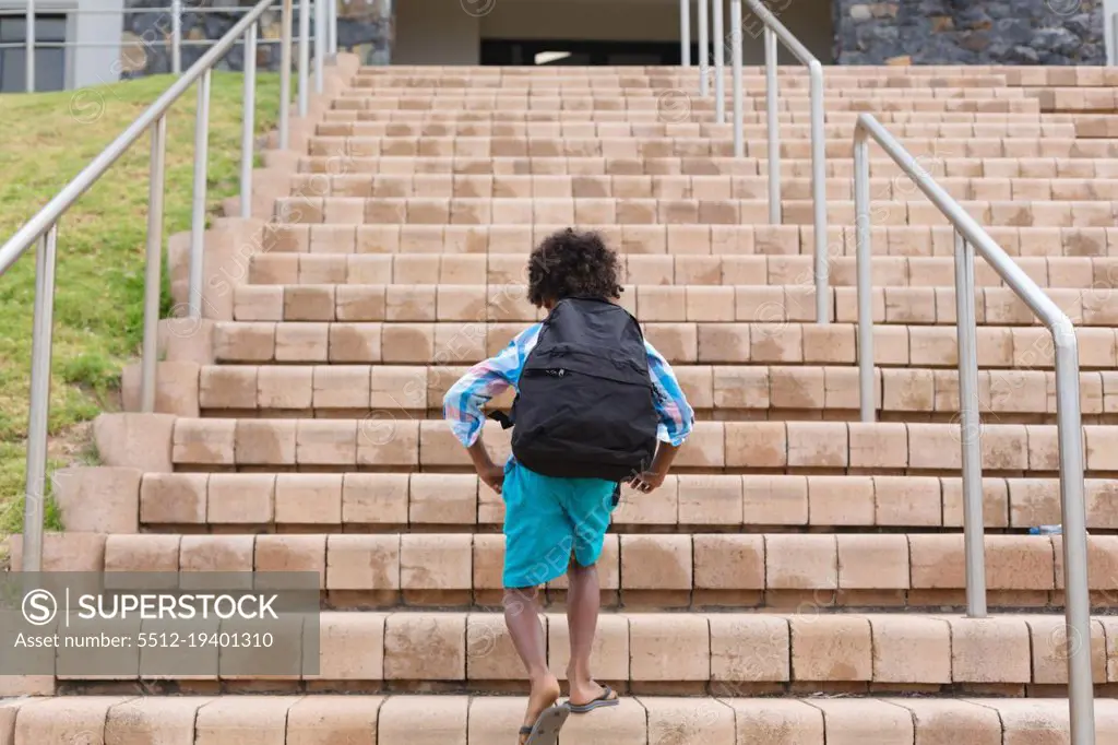 Rear view of african american elementary schoolboy with backpack climbing school building steps. unaltered, childhood, education and school concept.