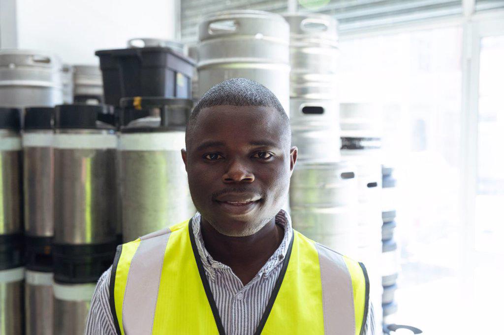 Portrait of an African American man working in a microbrewery, wearing high visibility vest and looking straight into a camera.