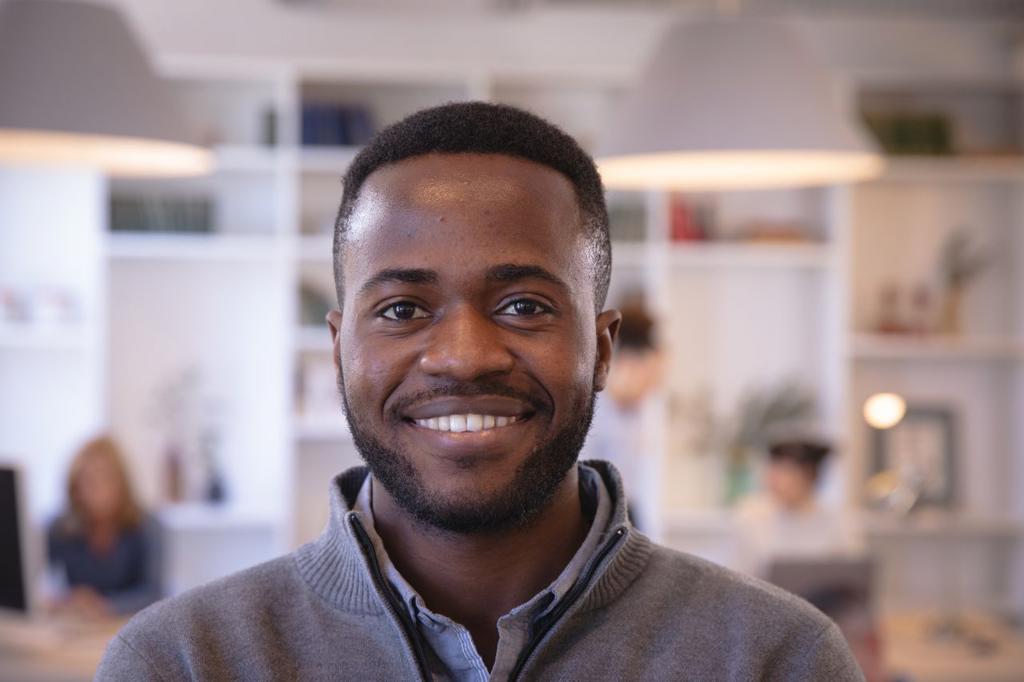 Portrait of a happy African American businessman working in a modern office, looking at camera and smiling, with his colleagues working in the background
