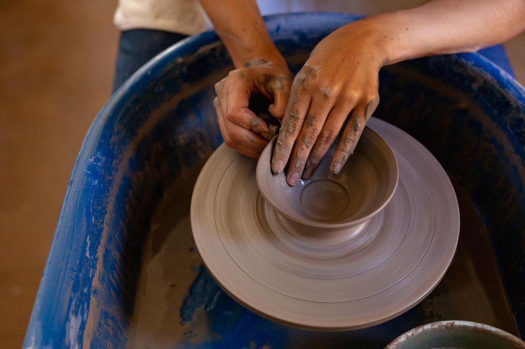 Elevated close up of the hands of a young Caucasian female potter shaping wet clay into a bowl shape on a potters wheel in a pottery studio