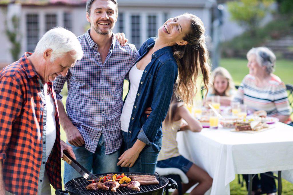 Couple and a senior man at barbecue grill preparing a barbecue in garden