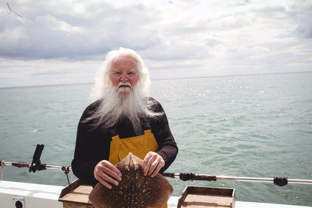 Portrait of fisherman holding ray fish on boat