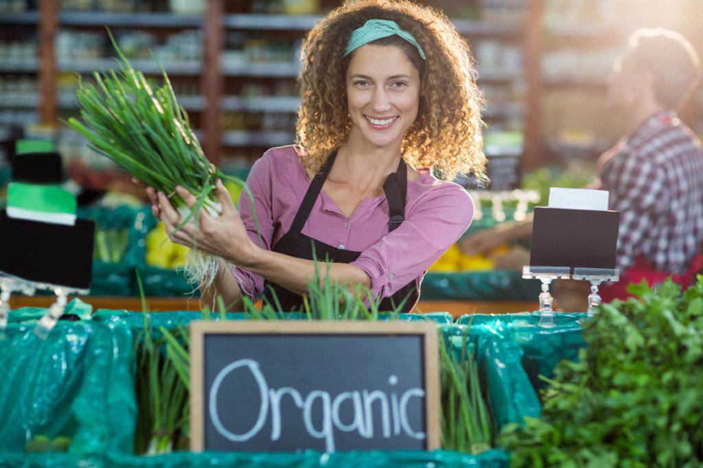 Portrait of smiling staff holding vegetable in organic section of supermarket