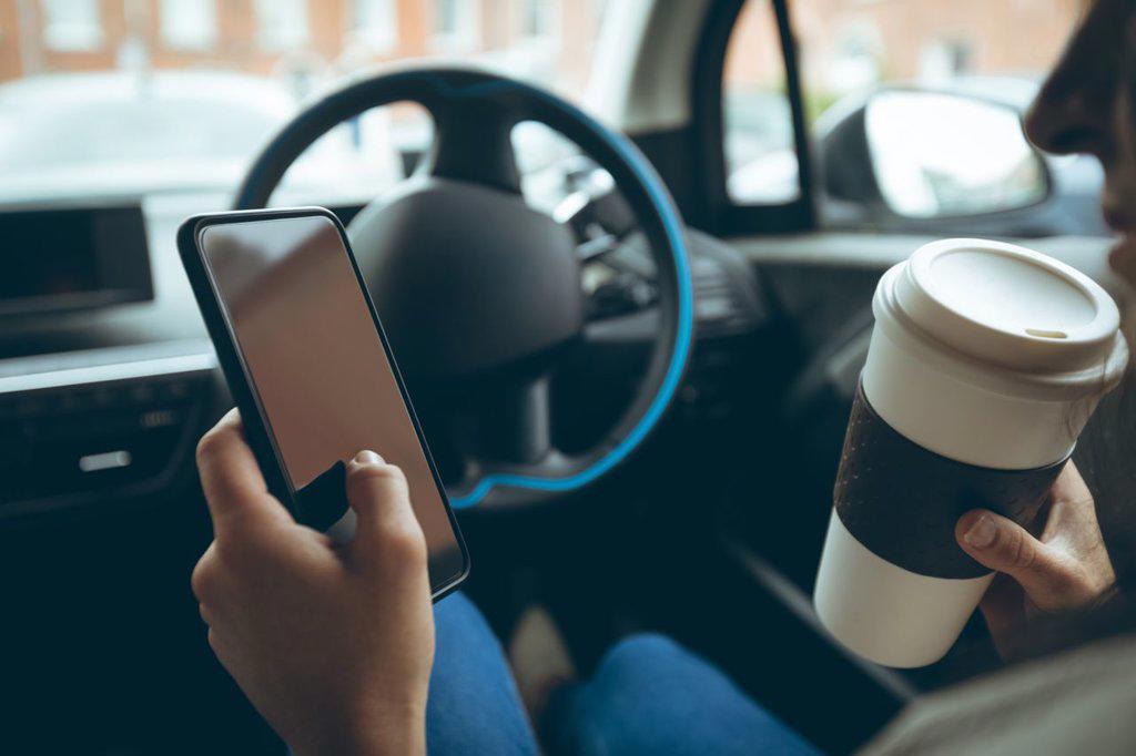 Businesswoman using mobile phone while having coffee in a car