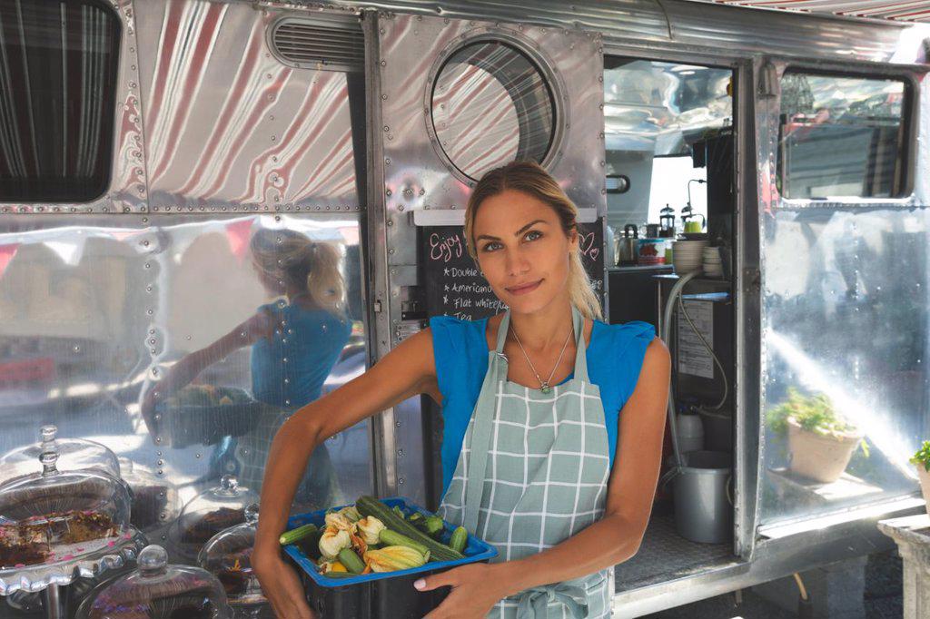 Female waitress holding vegetables in basket near food truck