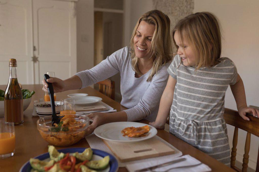 Mother serving food to her daughter on dining table at home