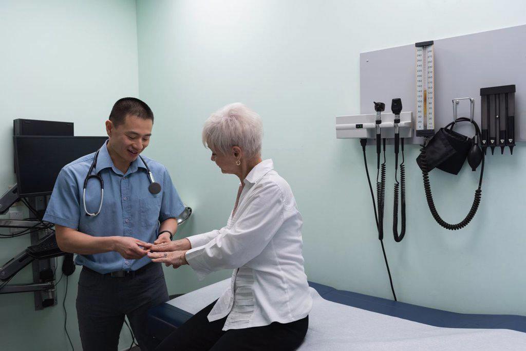 Young Asian male doctor examining a senior patient in the clinic while touching her hands