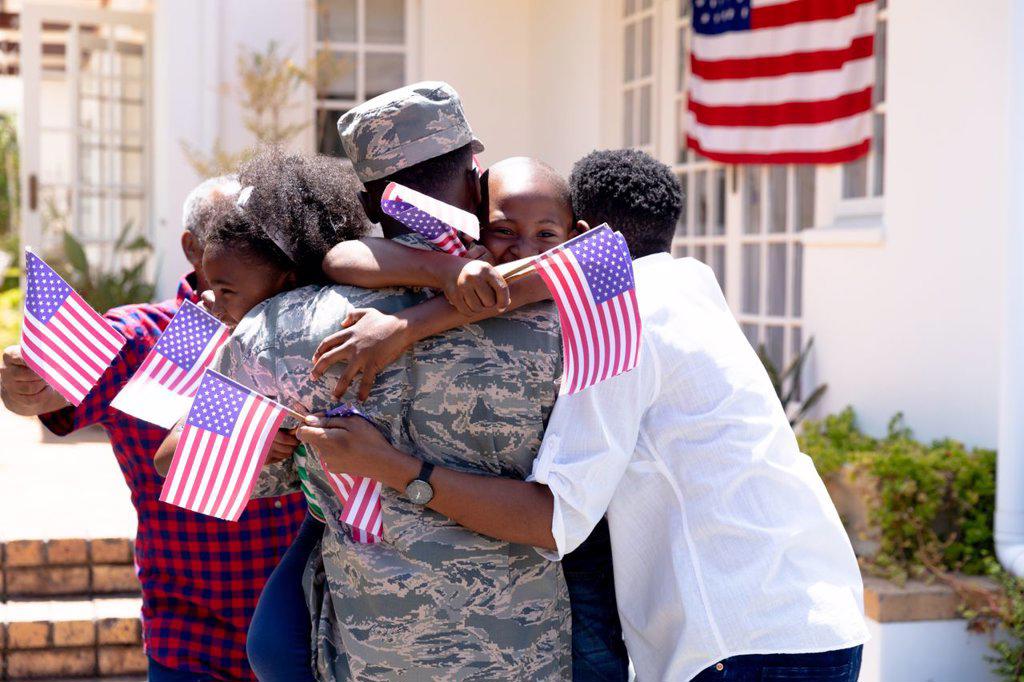 African American three generation family standing by their house, welcoming an African American solider wearing uniform, embracing and interacting.