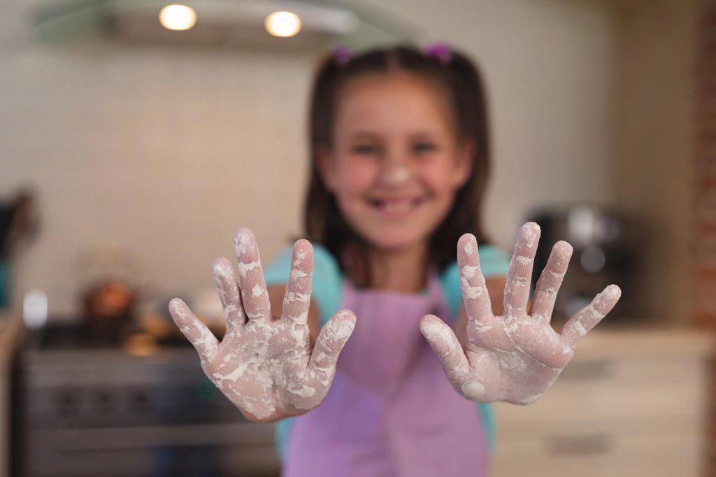 Portrait of caucasian girl in a kitchen, looking at camera and showing her hands with flour. self isolation at home during coronavirus covid 19 quarantine lockdown.