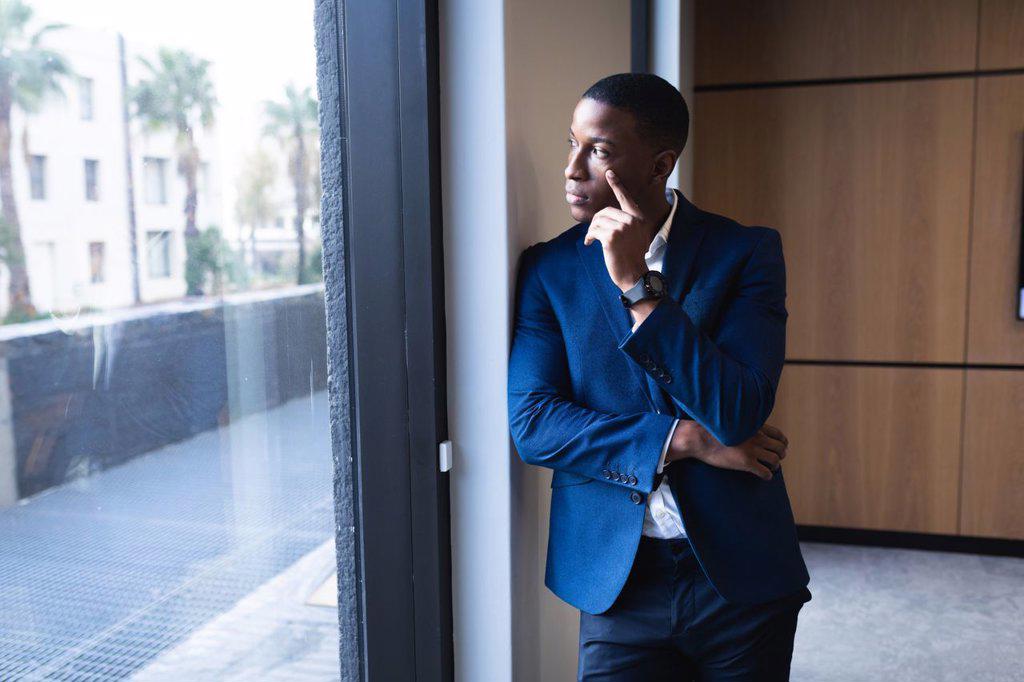 Thoughtful african american businessman looking out of window at modern office. business and office concept