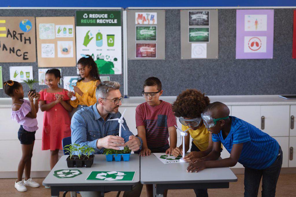 Caucasian male teacher holding windmill model teaching group of diverse boys in environment class. school and education concept
