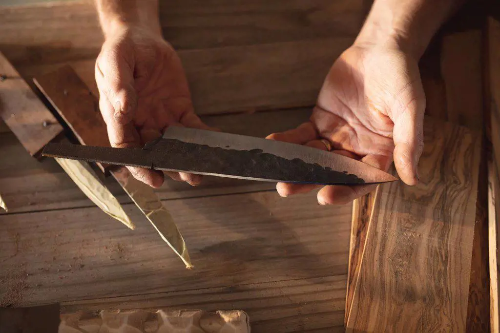 Hands of caucasian male knife maker in workshop, holding handmade knife. independent small business craftsman at work.