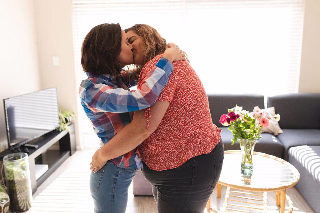 Happy lesbian couple embracing and kissing in living room. domestic lifestyle, spending free time at home.