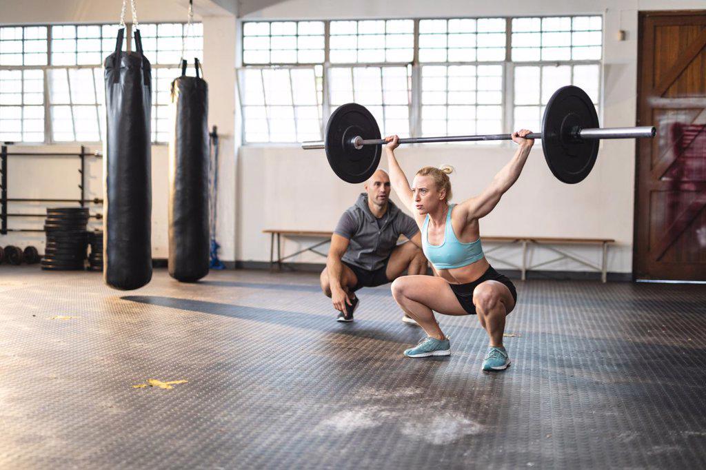 Caucasian male trainer instructing woman exercising at gym, lifting weights. strength and fitness cross training for boxing.