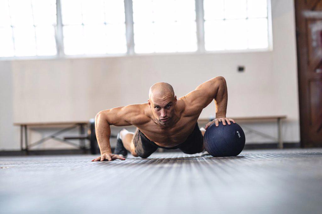 Strong caucasian man exercising at gym, doing push-ups using ball. strength and fitness cross training for boxing.