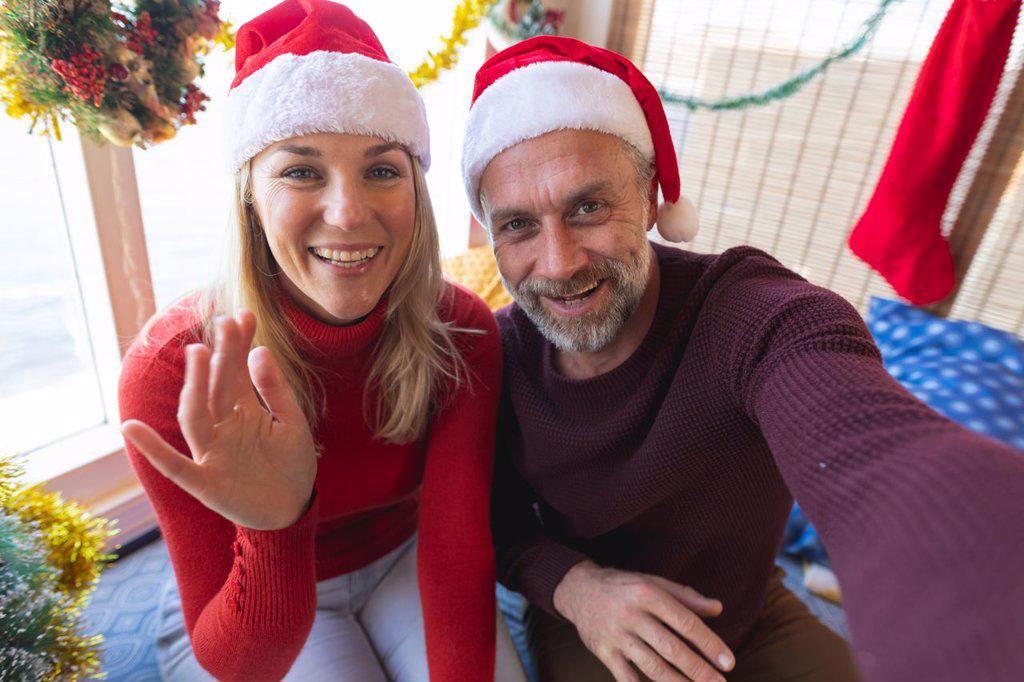 Happy caucasian mature couple wearing santa hats making a video call at christmas. christmas, festivity and communication technology.