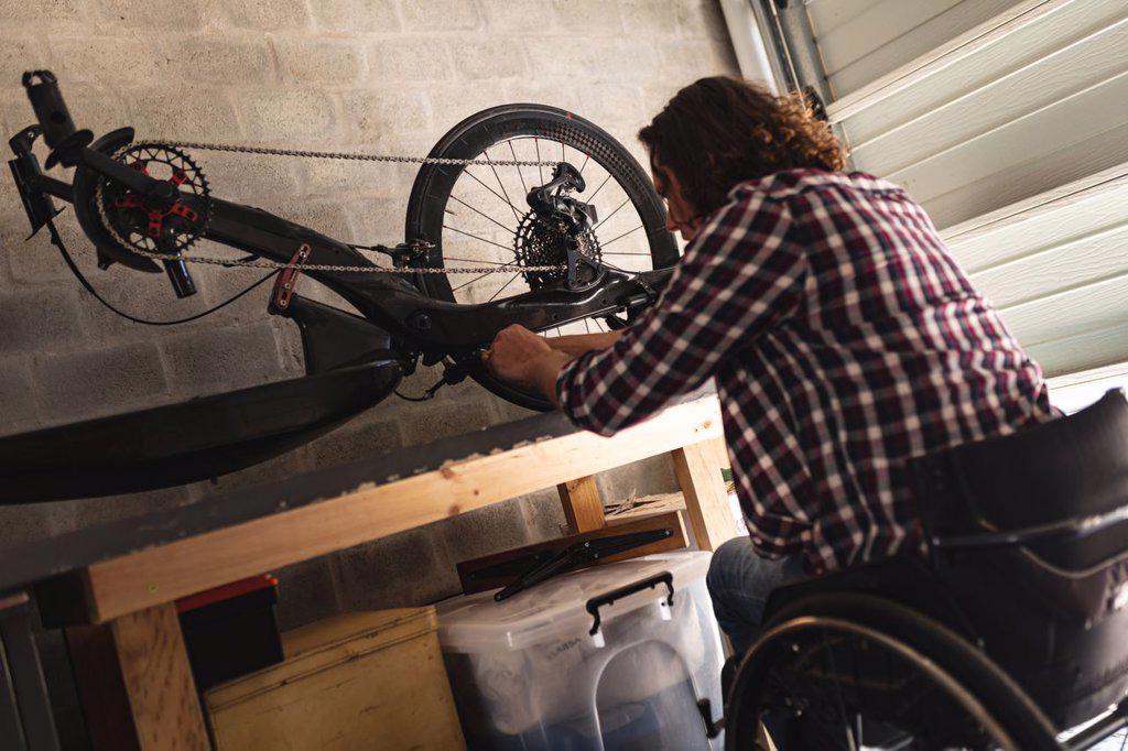Caucasian disabled man sitting on wheelchair repairing another wheelchair at home. disability and handicap concept