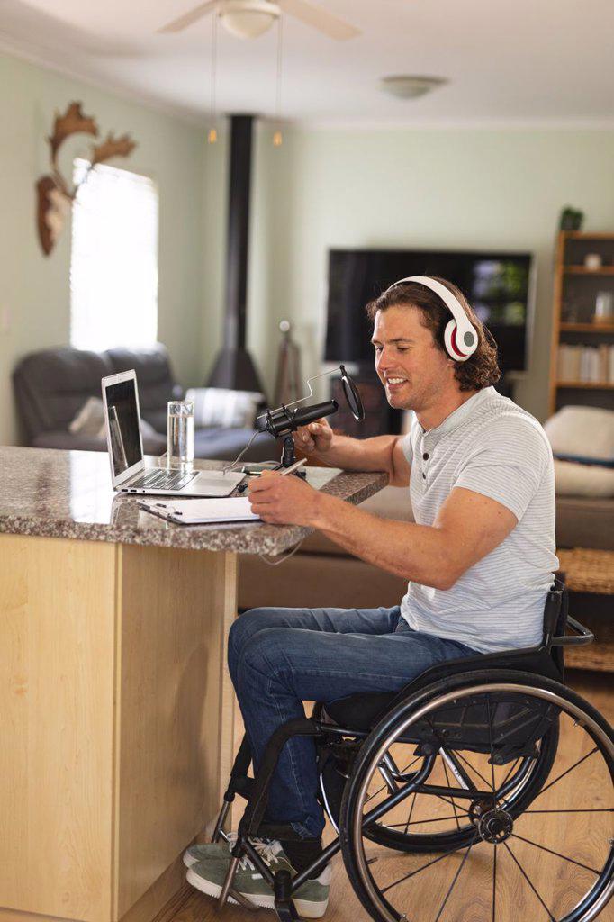 Caucasian disabled man recording podcast using microphone sitting at home. blogging, podcast and broadcasting technology concept