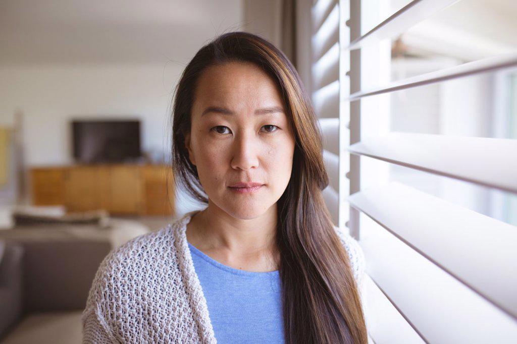 Portrait of serious asian woman standing at window, looking at camera. lifestyle, leisure and spending time at home.