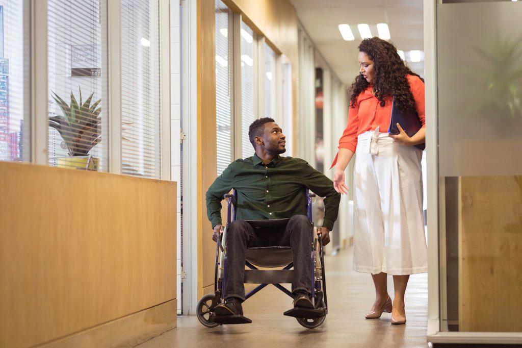 Affrican american businessman in wheelchair talking with biracial businesswoman in modern office. business and office workplace.